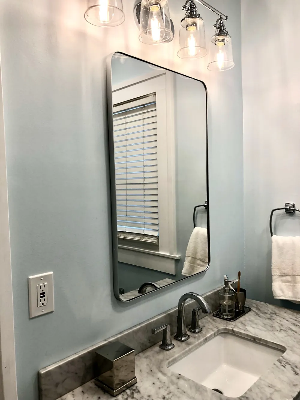 A framed mirror, glass sconces and a stone vanity top