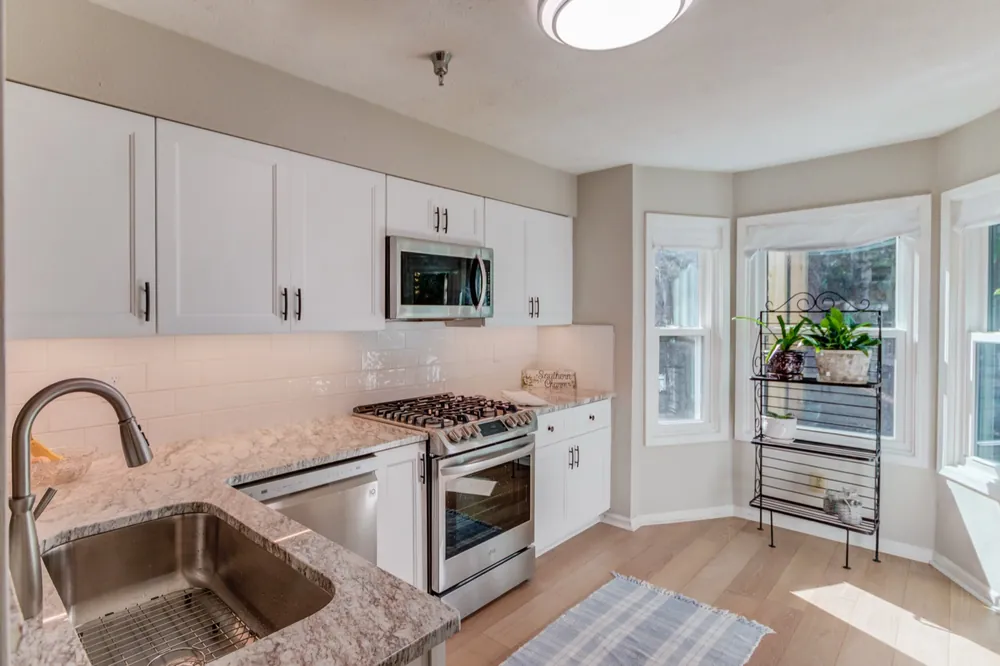 White cabinets, granite counters and a gas range near a bay window